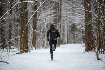 Photo from back of running athlete among trees in winter forest