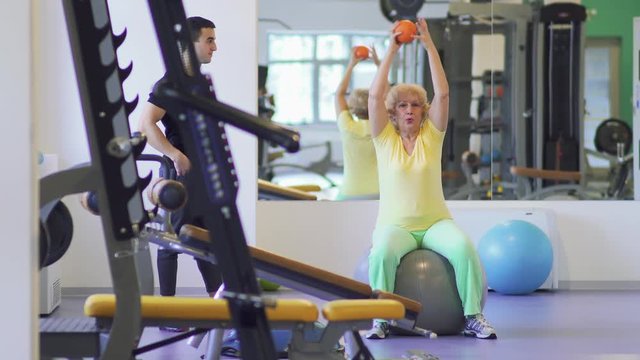 Elderly woman makes fitness exercise with ball in the gym