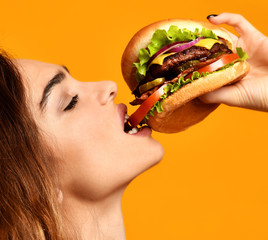 Woman eat burger sandwich with hungry mouth on yellow background