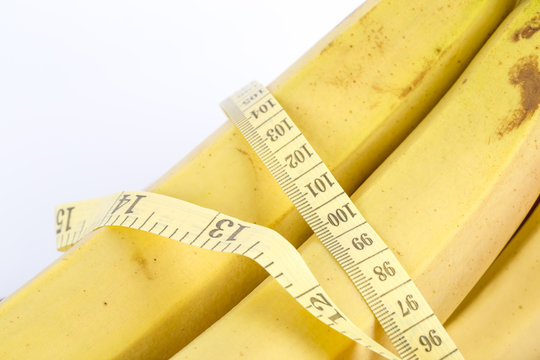 Ripe banana and measuring tape on the white background. Healthy lifestyle - fruit food, sport exercising.