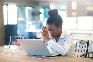 Tired black female praying near laptop