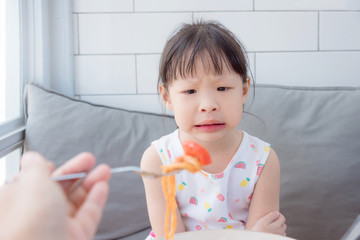 Little asian girl refuse to eat tomato in spagethi from her mother - obrazy, fototapety, plakaty