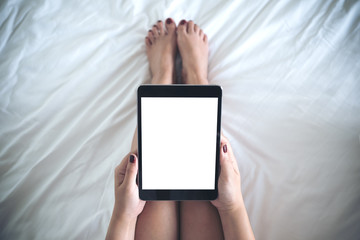 Top view mockup image of a woman holding black tablet pc with blank desktop white screen while sitting on a white bed background