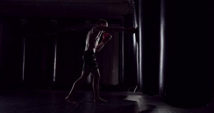 Boxer punching bag. Slow motion sequence. Strong athlete hits a punching bag. Kickboxing men training punching bag in fitness studio. Fighter Training Slow Motion