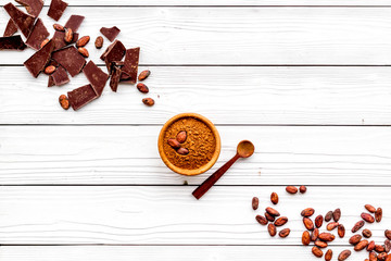 Chocolate and cacao concept. Cocoa powder in bowl near cocoa beans and broken chocolate on white background top view copy space