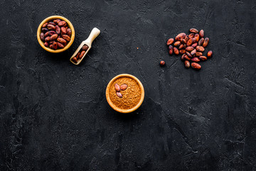 Cocoa powder in bowl and cocoa beans on black background top view copy space. Popular ingregients for sweets, bakery, drinks