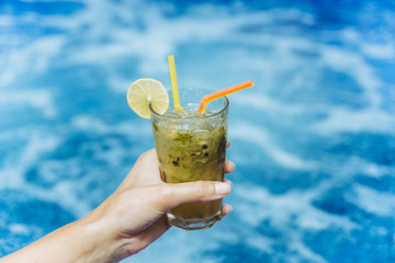 Cocktail in woman's hand near swimming pool close up