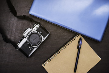 Vintage camera and computer notebook and notebook on wood background.