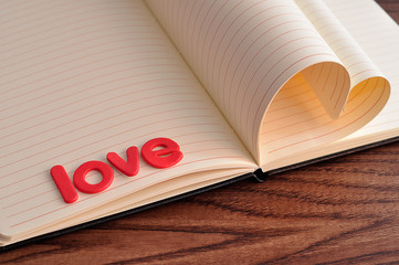 Pages of a book bend in a heart shape displayed with the word love