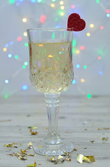 A glass of champagne with a red heart against an out of focus light background