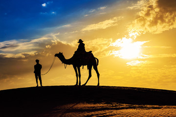 Thar Desert sunset at Jaisalmer Rajasthan with tourist on camel in silhouette effect and moody sky.	