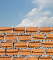 Red brick wall against blue sky with cloud.