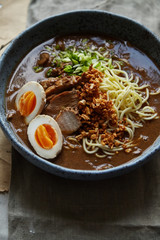 Close up of japanese ramen with pork belly, mushrooms and marinated eggs served in blue handmade ceramic bowl garnished with chives