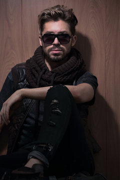 relaxed fashion man in sunglasses sits on wood in studio