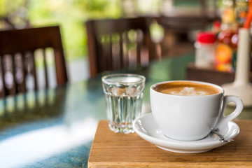 Hot Coffee Latte in white cup with water in a glass on the wooden table with space in the left side