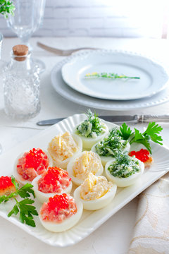 Stuffed eggs - with red fish, cheese and green cucumber on a white plate, selective focus