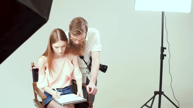 A beautiful model is signing an agreement with photographer in a studio before shooting.
