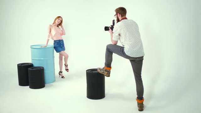 Beauty model is posing in studio near big blue barrel. Wearing short jeans skirt and pink T-shirt.