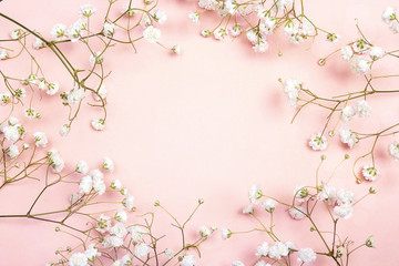 Frame of delicate little white flowers on pink background from above. Space for text.