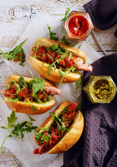 Delicious fresh hot dogs in homemade buns with arugula and ketchup on a wooden background.