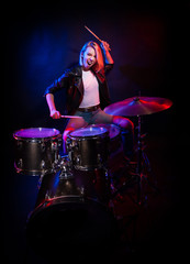 Fototapeta na wymiar A blonde girl in a leather jacket with drums on a black background.