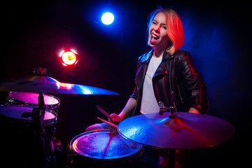 A blonde girl in a leather jacket with drums on a black background.