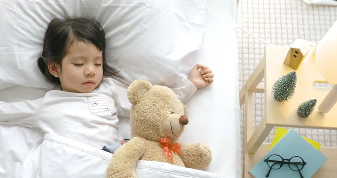 Child girl sleeping with teddy bear on the wooden bed in her bedroom, Happy asian child little girl with her teddy bear, family concept at home