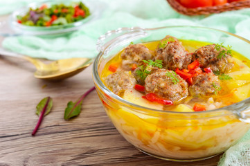 Rice soup with meat balls and vegetables in a transparent glass bowl. Close up