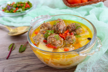 Rice soup with meat balls and vegetables in a transparent glass bowl. Close up