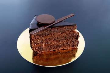 A piece of chocolate cake with chocolate cream on a golden napkin on a black background.