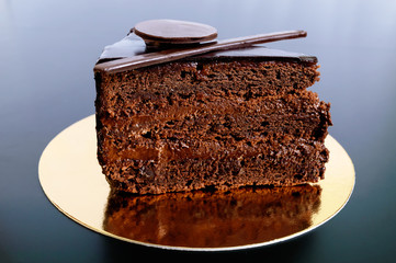 A piece of chocolate cake with chocolate cream on a golden napkin on a black background.