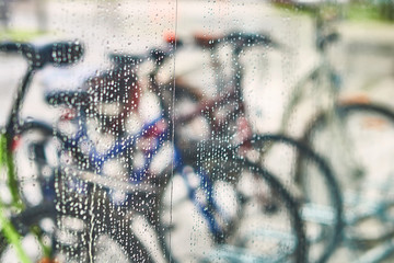 View of parked bicycles through the wet window glass with drops of water