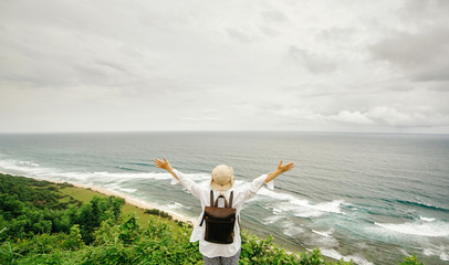 Travel and freedom. Young woman in hat with rucksack enjoying view of the ocean, waves and sky.