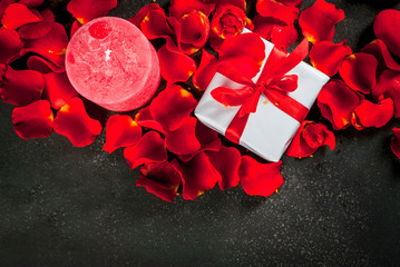 Valentine's day concept, with rose flower petals and white wrapped gift box with red ribbon, on dark stone background, copy space top view