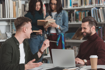 smiling students talking and sitting at table in library