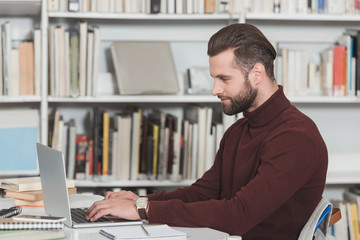 Obraz premium side view of handsome student using laptop in library