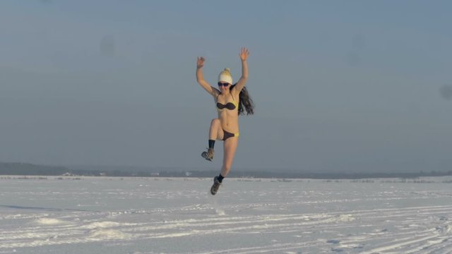 A woman in a swimsuit runs and jumps on a snowy day. 