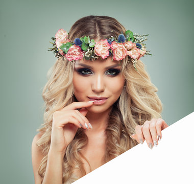 Spring Woman with Flowers Hairstyle Holding White Banner for Text. Blonde Beauty. Fashion Model with Long Permed Curly Hair and Perfect Makeup