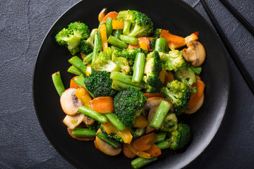 Hot stir fried vegetables on black plate. Healthy asian food concept.