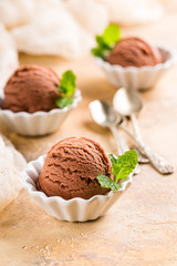 Chocolate ice cream scoop in white bowl with mint leaves on sand color stone background. Summer food concept with copy space.