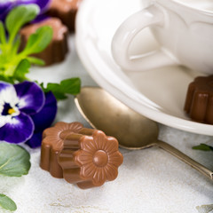 Chocolate candies in flower shape with violets and cup of coffee. Holiday food concept with copy space.