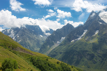 Fototapeta premium summer landscape of the Caucasus mountain peaks, green slopes in the grass with snow-capped peaks against the blue sky with clouds