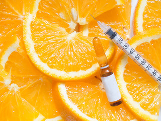 High dose vitamin C brown ampule for injection with syringe on fresh juicy orange fruit slices....