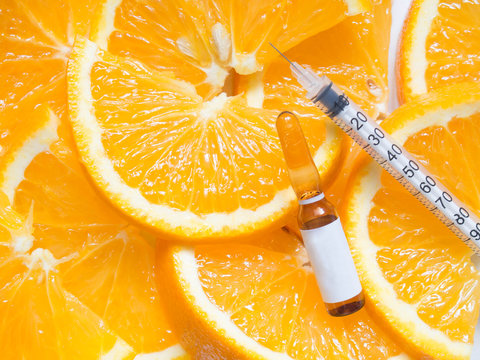 High dose vitamin C brown ampule for injection with syringe on fresh juicy orange fruit slices. Concept of vitamin/mineral supplement, beauty/cosmetic product and health nutrition. Copy space. 