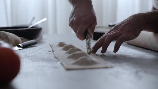 Man hand closeup cutting pasta ravioli with a pastry wheel.