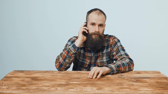 Hipster bearded man sitting at wooden table talking on mobile phone