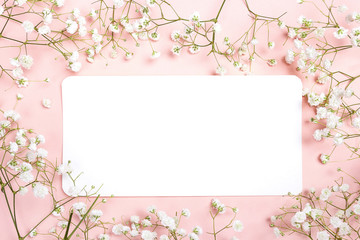 Obraz na płótnie Canvas Blank paper card with delicate little white flowers on pink background. Space for text.