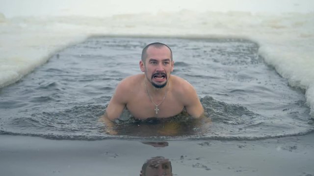 A man swims in an ice hole and stands to get outside. 