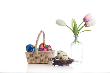 Osterarrangement mit Korb , traditionell bemalten Ostereiern, Osternest und Tulpen in einer Vase