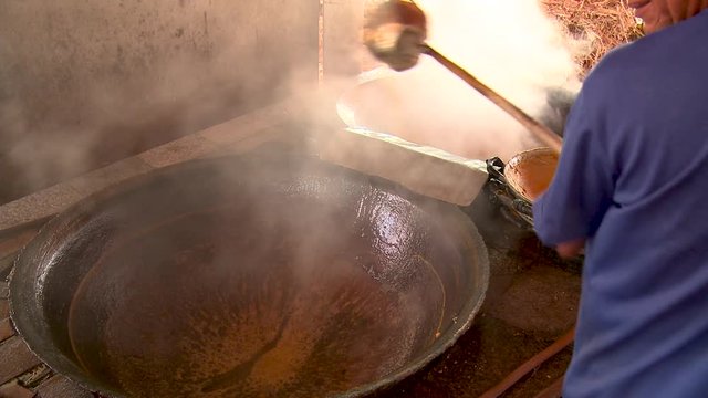 Man scoops sugar cane juice from one heated vat to another